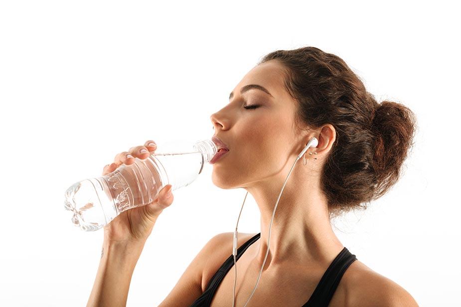 devojka sa slušalicama u ušima pije vodu posle sporta - pijenje vode