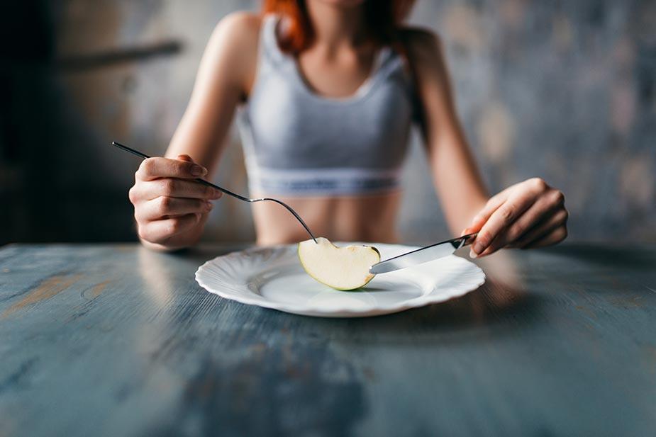 anorektična devojka ispred koje je tanjir sa malim parčetom jabuke