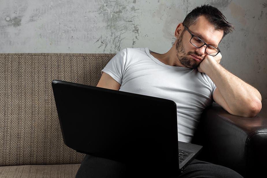mlađi čovek drema sa laptopom u krilu