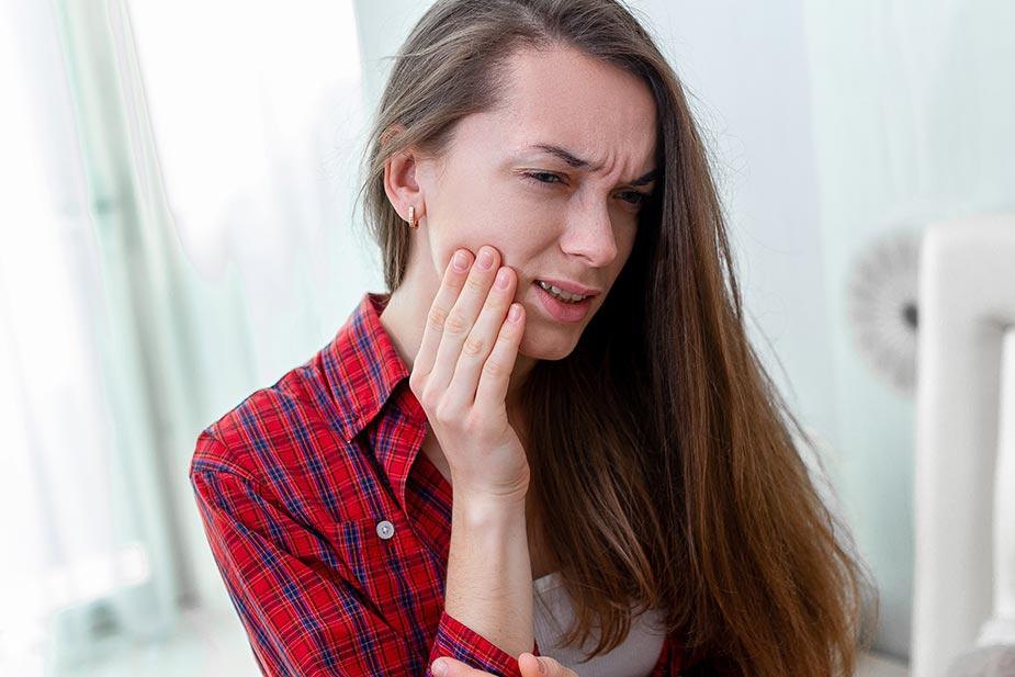 mlađa žena se drži za obraz jer je muči paradentoza (paradentopatija))
