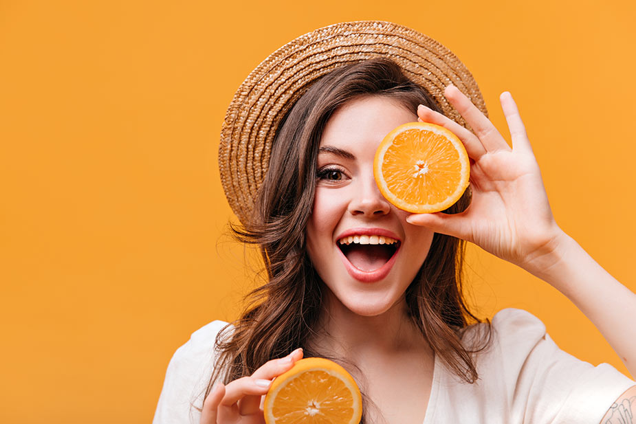 Nasmejana devojka drži presečenu narandžu na pola na oku - Vitamin C