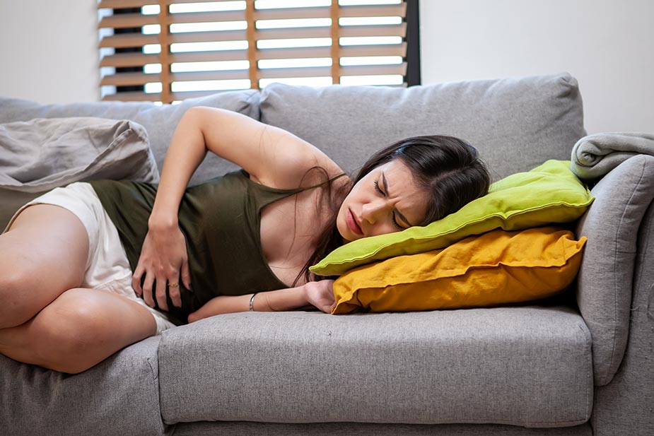 Mlađa žena zgrčena na kauču drži se za stomak