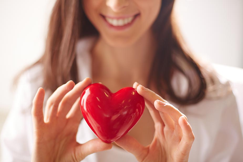 Mlada nasmejana žena drži plastični model srca