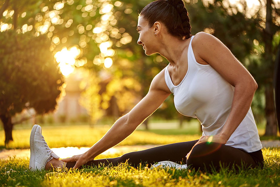 Mlađa žena se isteže na travi pre trčanja