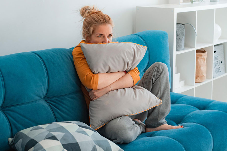 Nezadovoljna žena sedi na plavom kauču sa jastukom preko lica.