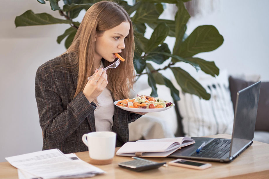 Poslovna žena jede zdrav obrok na radnom mestu gledajući u monitor
