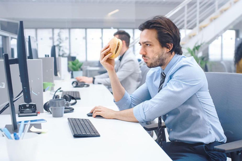 Poslovni čovek jede brzu hranu na radnom mestu gledajući u monitor.