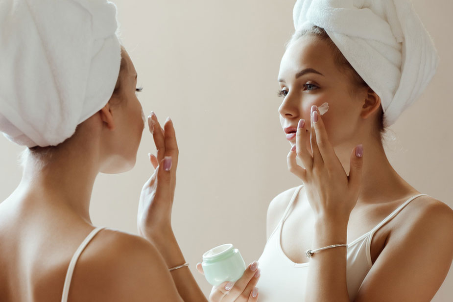 Žena nanosi kremu na lice ispred ogledala