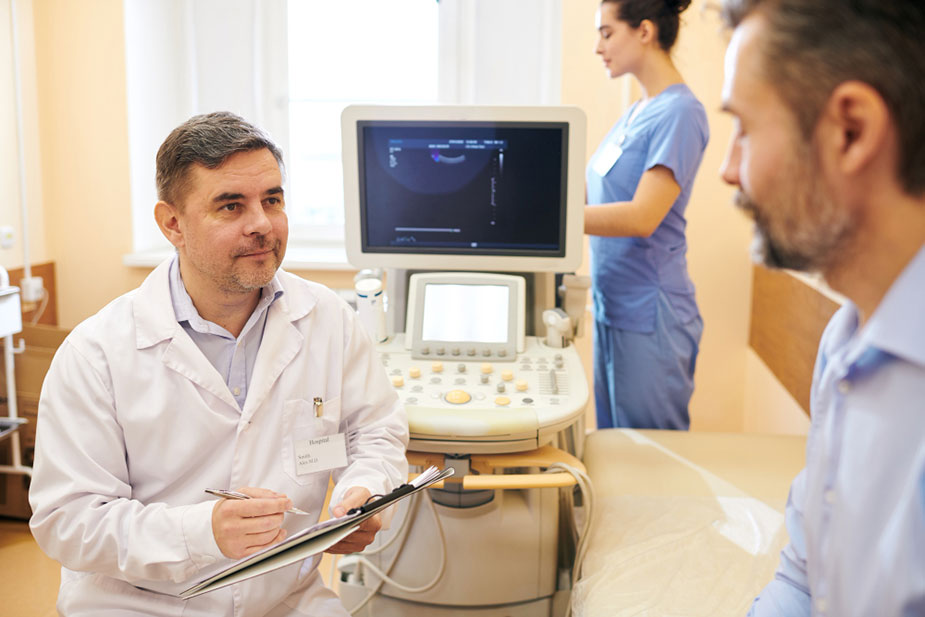 Lekar razgovara sa pacijentno, u pozadini se vidi medicinska sestra i uređaj za ultrazvučni pregled