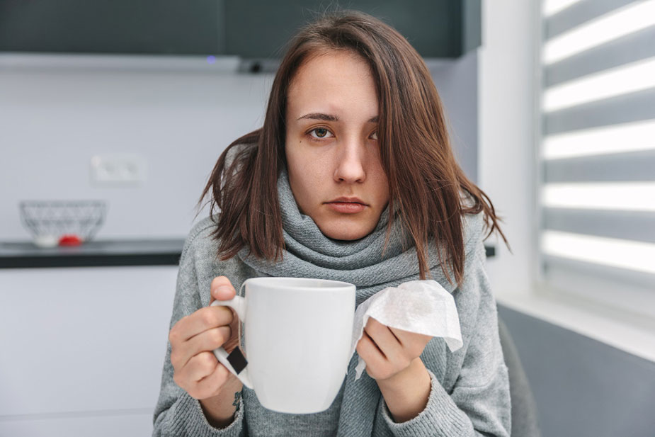 Žena sa prehladom u jednoj ruci drži šolju sa čajem a u drugoj maramicu