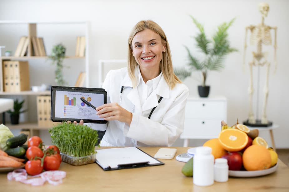 Nutricionista pokazuje grafikon na tabletu - oko nje na stolu su različite namirnice i suplementi
