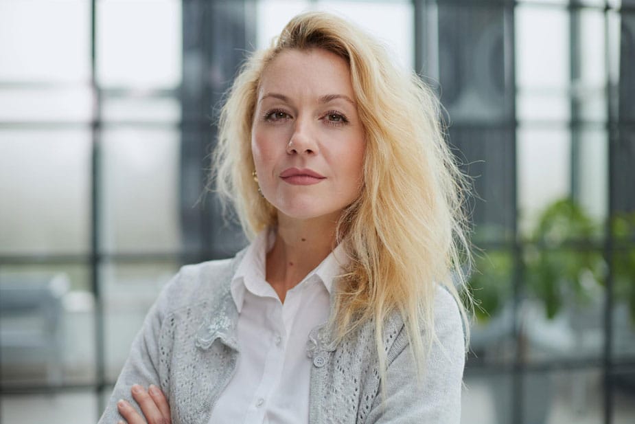 Žena u četrdesetim prekrštenih ruku zamišljeno gleda u pravcu kamere.