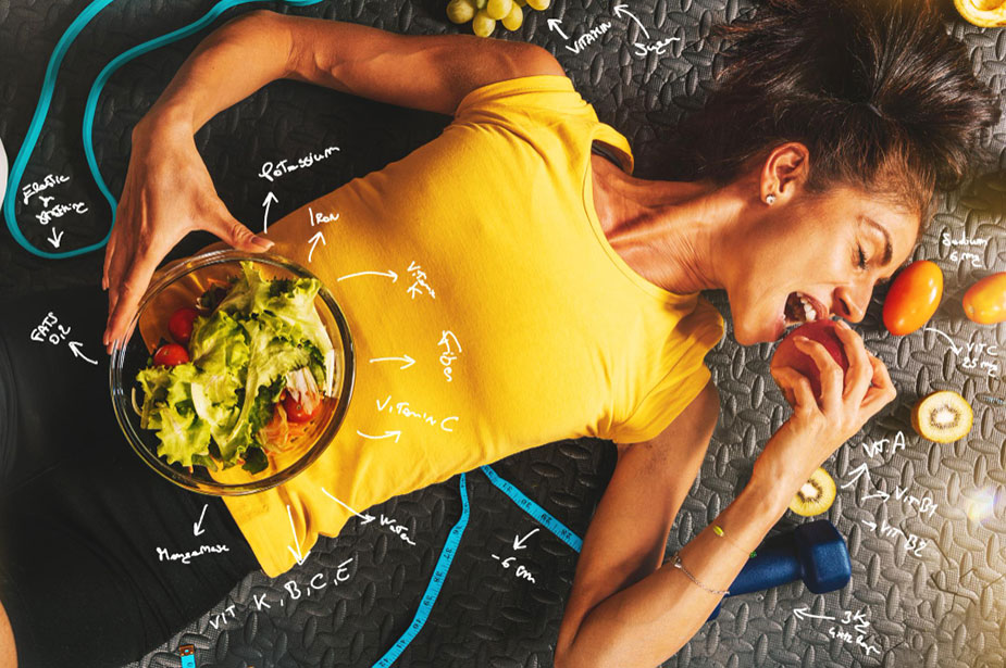 Žena leži na podu sa činijom zdrave hrane i gricka rotkvicu. Oko nje oprema za vežbanje.