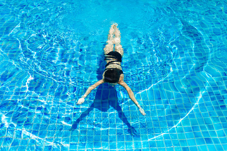 Osoba pliva u bazenu, izvodi prsni stil u bistroj plavoj vodi.