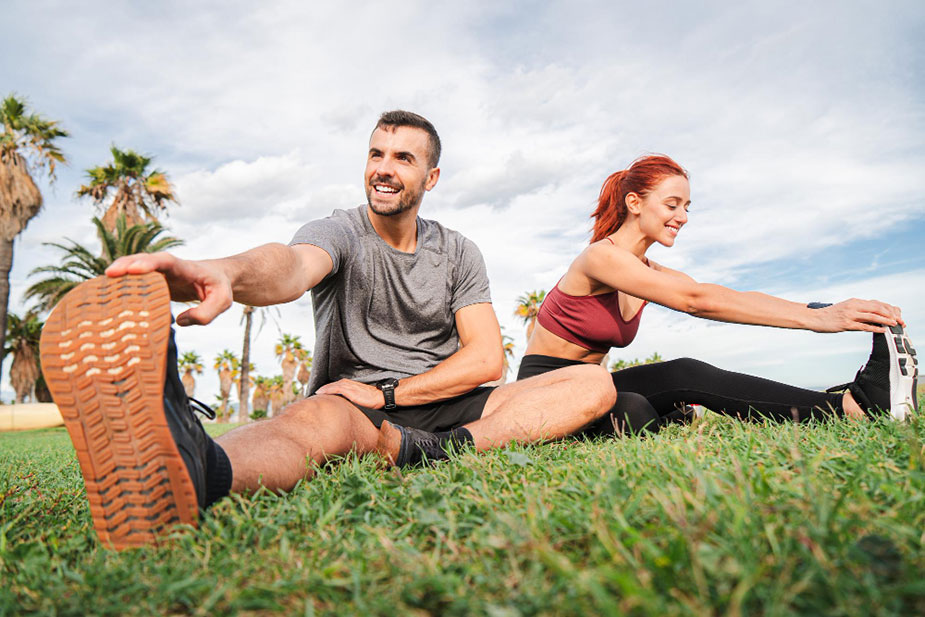 Muškarac i žena istežu se na otvorenom tokom sunčanog dana, sa palmama u pozadini.