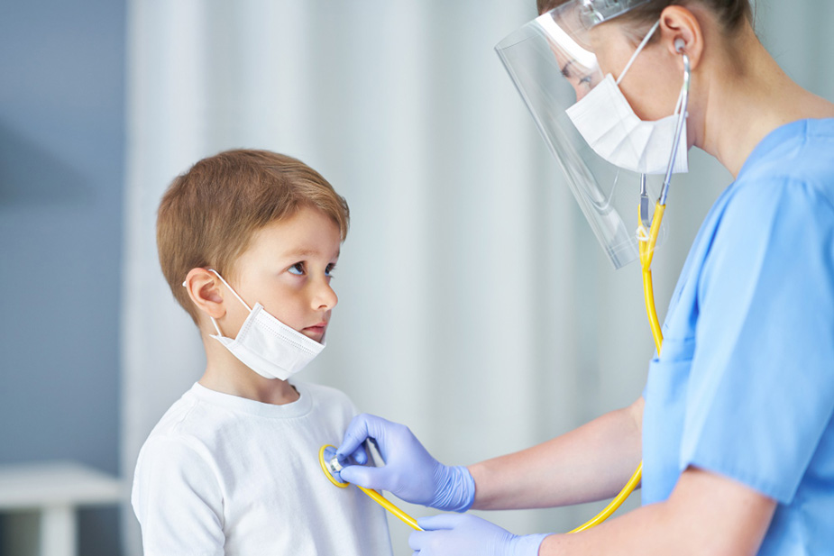 Lekar sa vizirom i maskom preko lica preslušava dečakova pluća