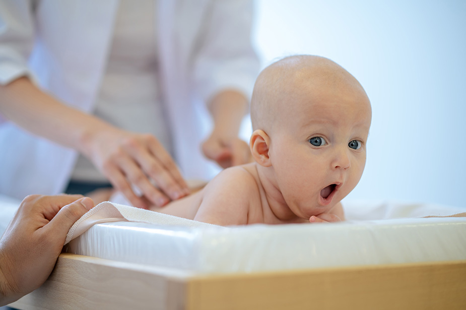 Iznenađena beba leži na stomaku dok je lekar pregleda.