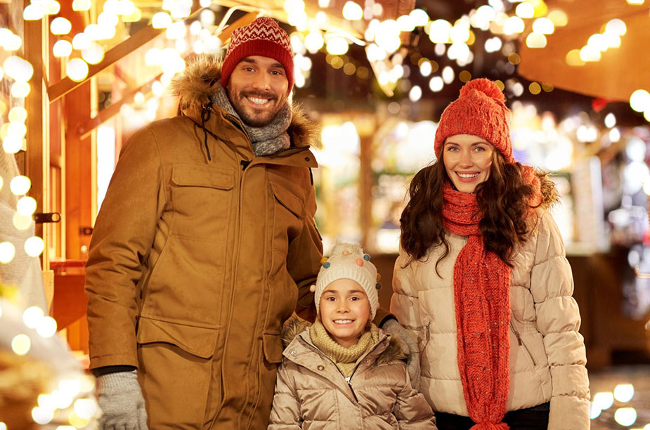 Porodica uživa u večernjoj šetnji tokom zime okružena prazničnim svetlima.