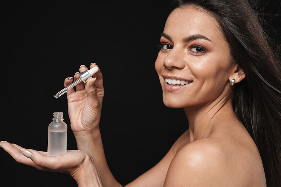 Nasmešena žena nanosi serum kapaljkom na kožu — primer bezbedne i pravilne kozmetičke rutine.