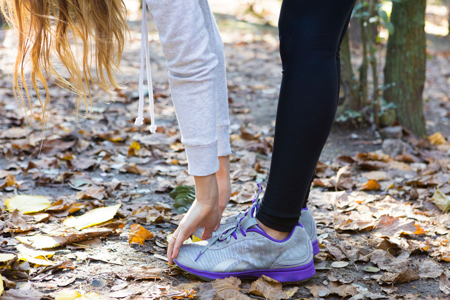 Osoba vezuje pertle na patikama pre šetnje na šumskoj stazi.