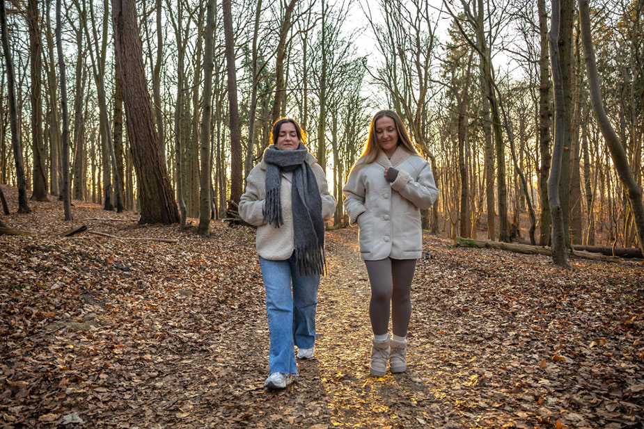 Dve žene šetaju stazom kroz park tokom hladnog dana.
