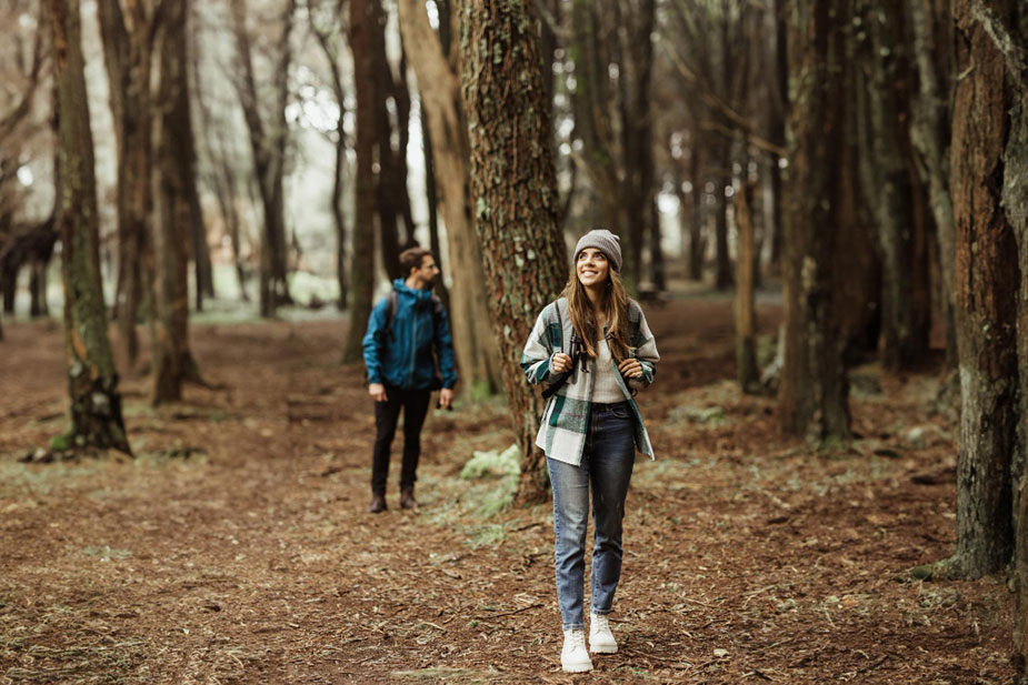 Žena u zimskoj garderobi šeta kroz šumu, dok je druga osoba u pozadini na stazi.