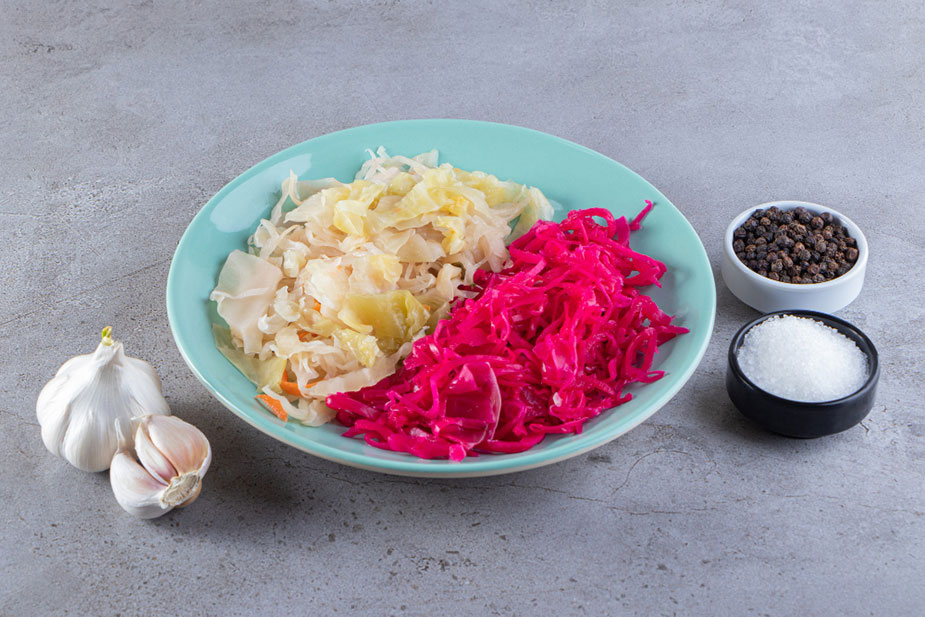 Kiseli kupus i kiseli crveni kupus na tanjiru, pored belog luka, soli i zrna bibera