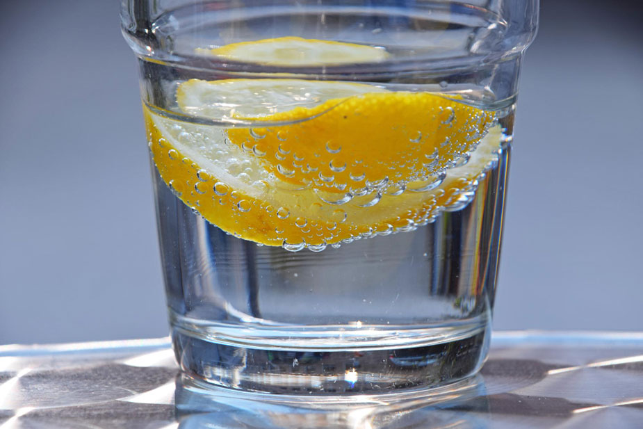 Čaša vode sa kriškom limuna i mehurićima u vodi