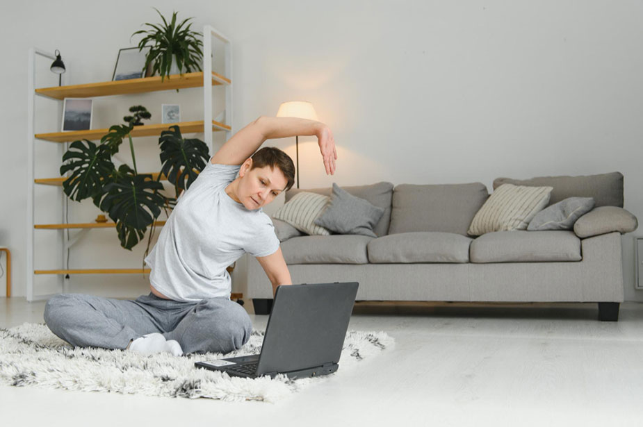 Osoba radi bočno istezanje trupa kod kuće, sedeći na tepihu pored