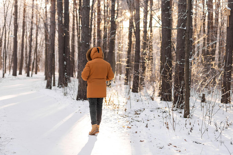 Osoba u narandžastoj zimskoj jakni hoda kroz snežnu šumu
