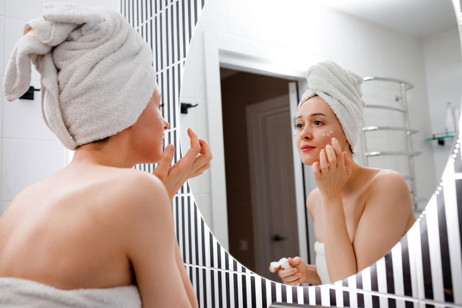 Žena nanosi kremu na lice ispred ogledala – jednostavna rutina hidratacije kože
