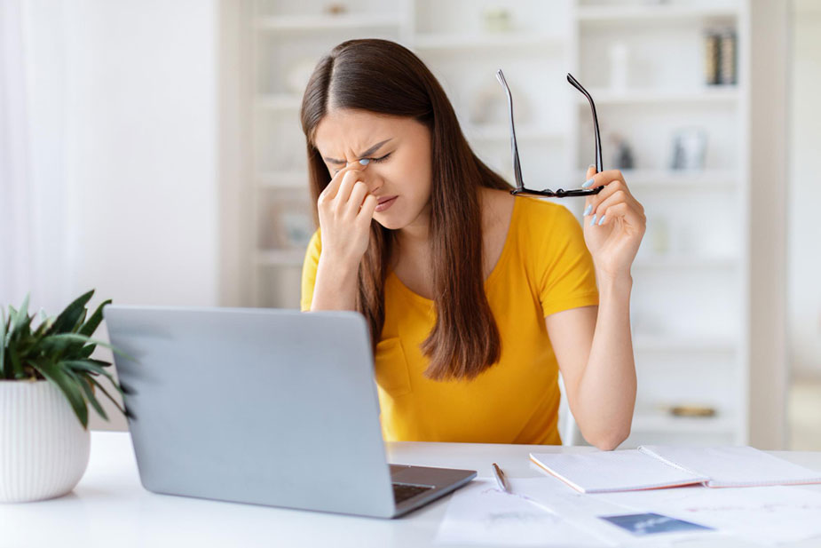 Žena za laptopom trlja oči i drži naočare – znakovi digitalnog zamora i suvih očiju