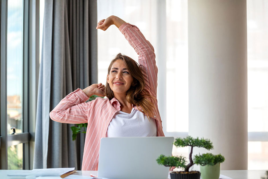 Žena za laptopom radi istezanje za vrat i ramena kao primer kratkog pokreta tokom sedentarnog rada