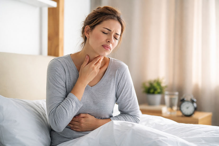 Žena se budi sa jutarnjim simptomima refluksa i drži ruku na grlu i stomaku